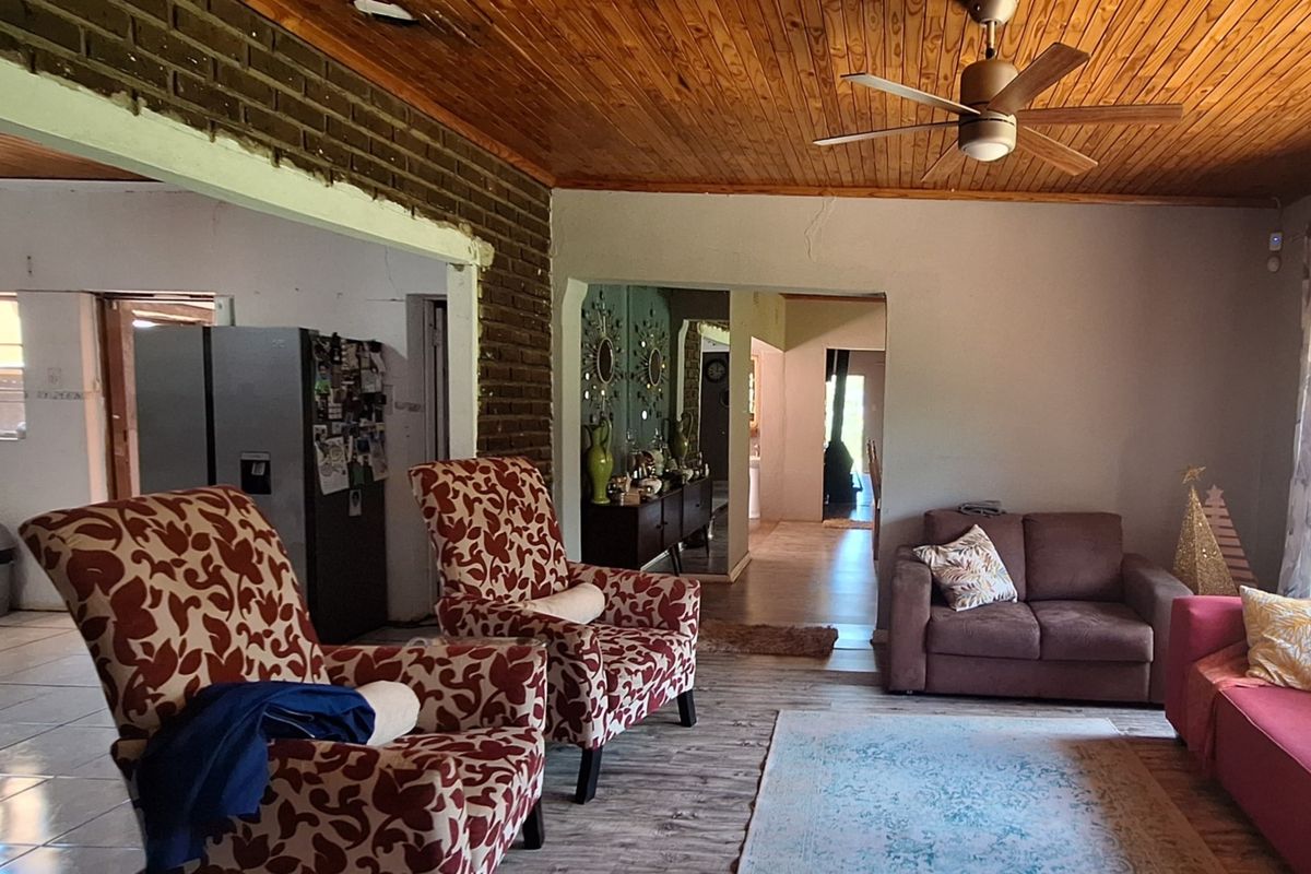 Spacious living area featuring exposed brickwork, a timber ceiling with a fan, and tiled flooring, offering a rustic aesthetic with potential for modernization.
