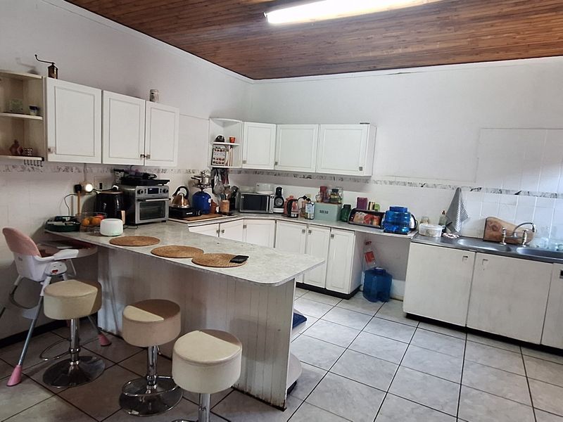 Functional kitchen featuring white cabinetry, laminate countertops, a breakfast nook, and tiled flooring with a traditional timber ceiling finish.