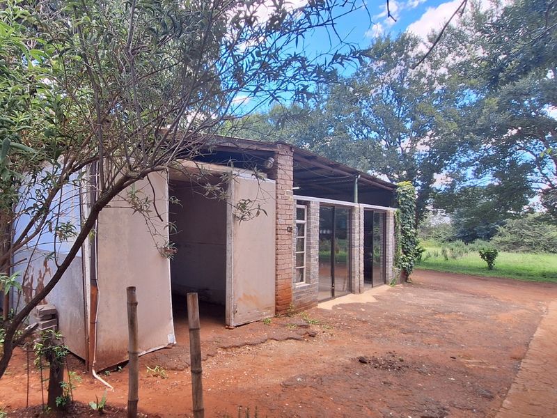 Rear view of a rustic outbuilding featuring brick masonry, sliding glass doors, and a corrugated metal roof set within a natural garden environment.
