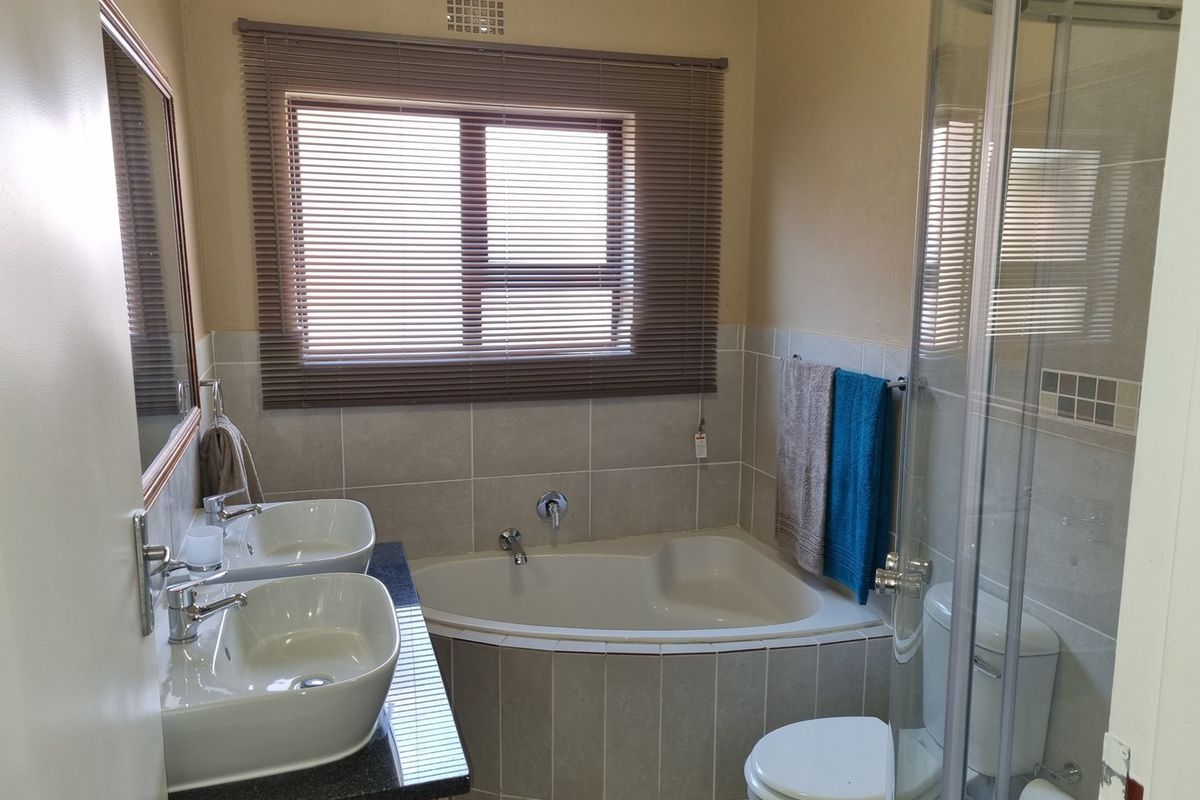 A well-appointed bathroom featuring a double vanity, corner bathtub, and a separate glass-enclosed shower with neutral tiling.