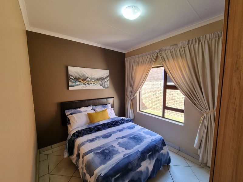 A well-maintained bedroom featuring tiled flooring, a built-in cupboard, and a large window with curtains, providing natural light and a view of the exterior.