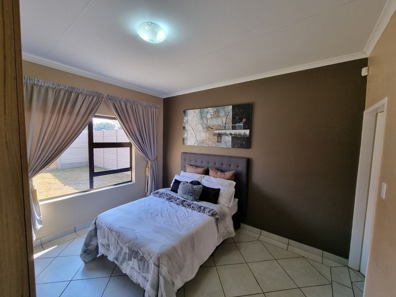 A well-maintained bedroom featuring tiled flooring, neutral wall tones, and an aluminium-framed window providing natural light.