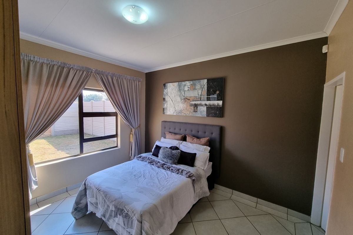 A well-maintained bedroom featuring tiled flooring, neutral wall tones, and an aluminium-framed window providing natural light.