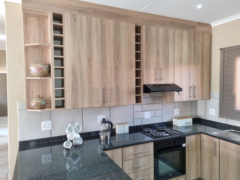 Modern kitchen featuring light wood-grain cabinetry, dark granite countertops, built-in oven, electric hob, and a tiled backsplash.