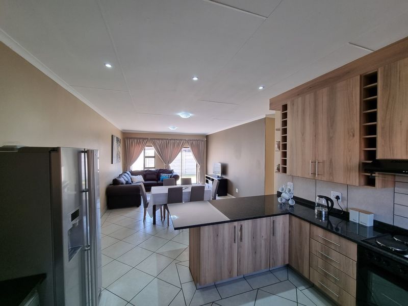 Open-plan living and dining area featuring a modern kitchen with wood-finish cabinetry, granite countertops, and tiled flooring throughout.