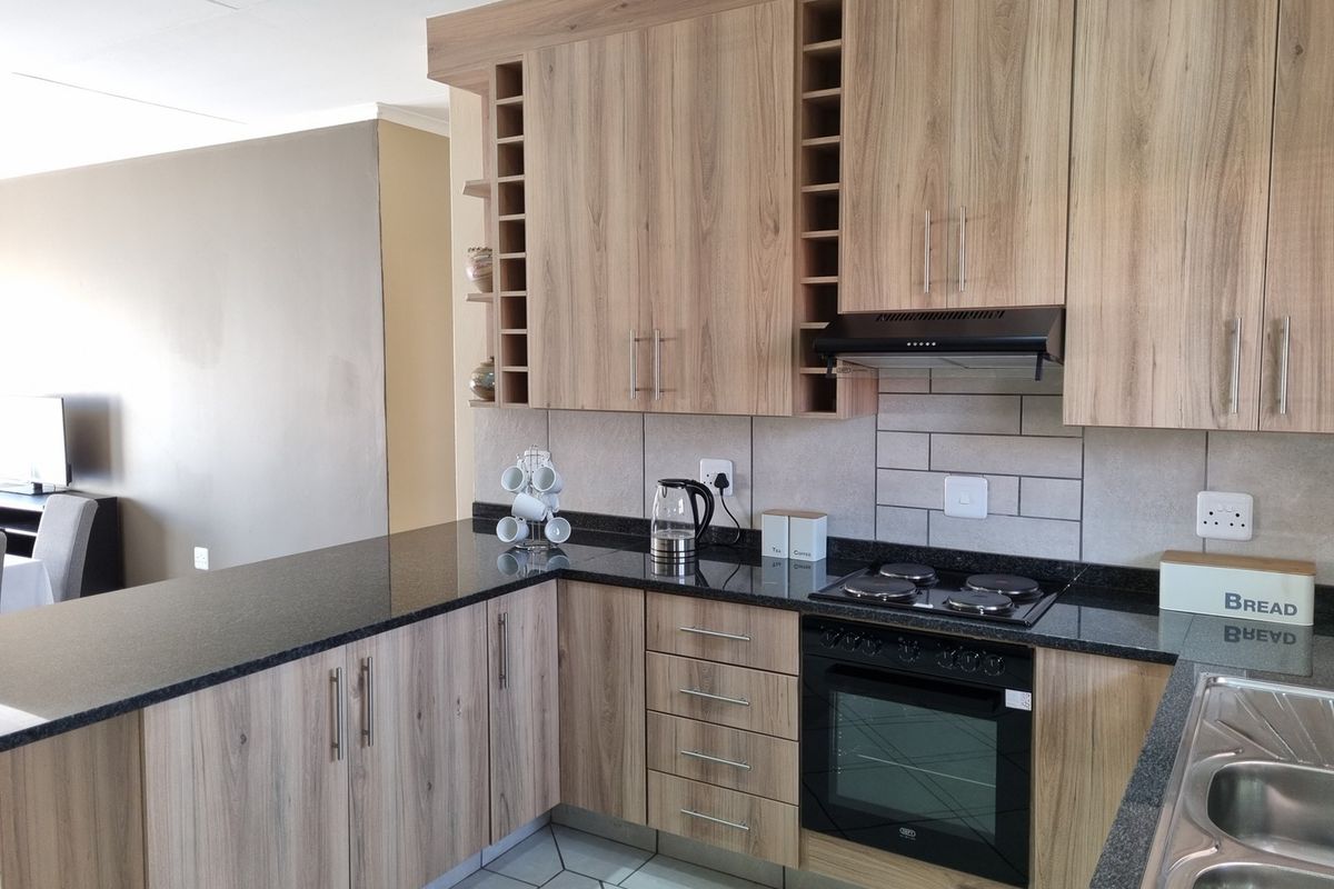 Modern kitchen featuring wood-look laminate cabinetry, granite countertops, subway tile backsplash, and integrated appliances including an oven and hob.