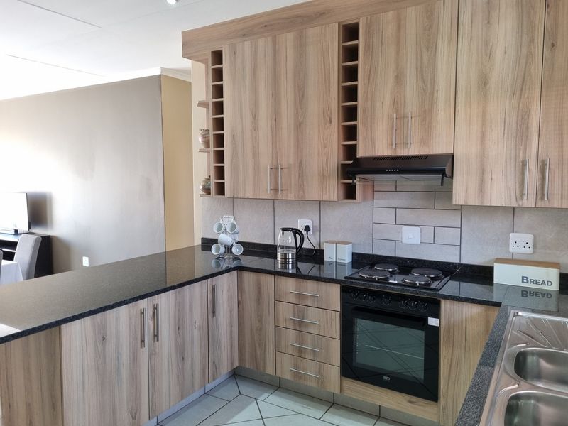 Modern kitchen featuring wood-look laminate cabinetry, granite countertops, subway tile backsplash, and integrated appliances including an oven and hob.