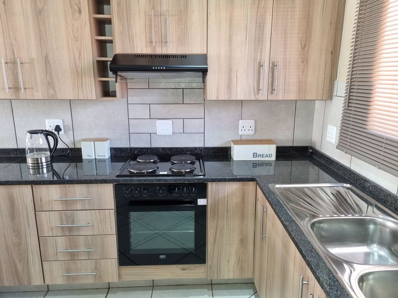 Modern kitchen featuring wood-look cabinetry, granite countertops, a built-in oven with electric hob, extractor fan, and a stainless steel double sink.