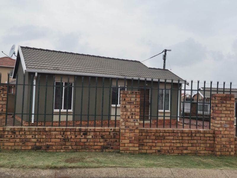 Front view of a detached house featuring a tiled roof, painted exterior walls, and a secure brick boundary wall with metal fencing.
