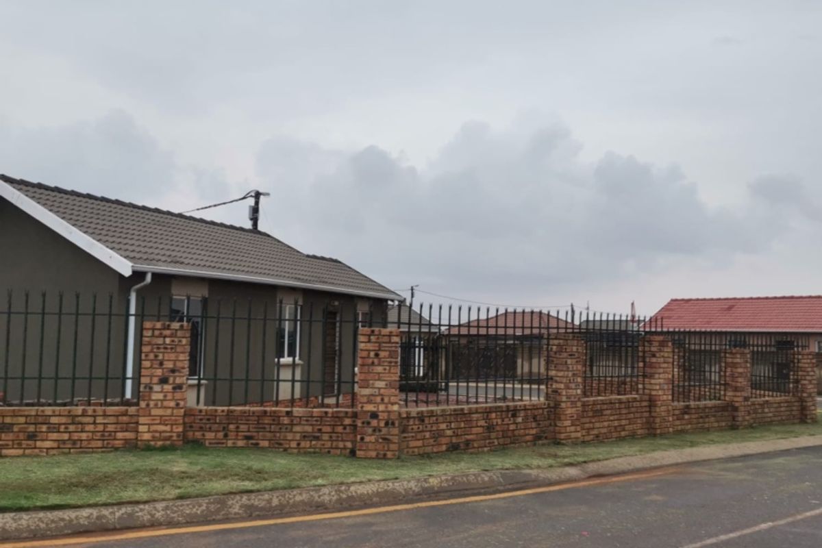 Front exterior view of a single-story house featuring a brick boundary wall with metal security fencing and a tiled roof.