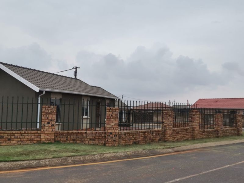 Front exterior view of a single-story house featuring a brick boundary wall with metal security fencing and a tiled roof.