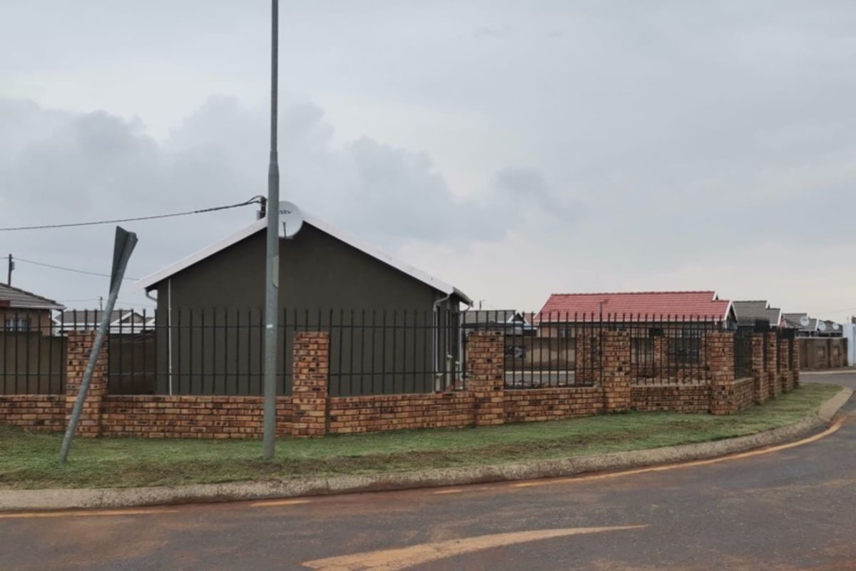 A street-level view of the property featuring a brick boundary wall with metal fencing and a satellite dish mounted on the exterior wall.