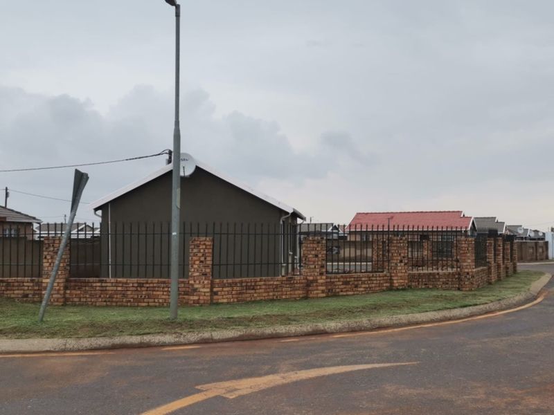 A street-level view of the property featuring a brick boundary wall with metal fencing and a satellite dish mounted on the exterior wall.