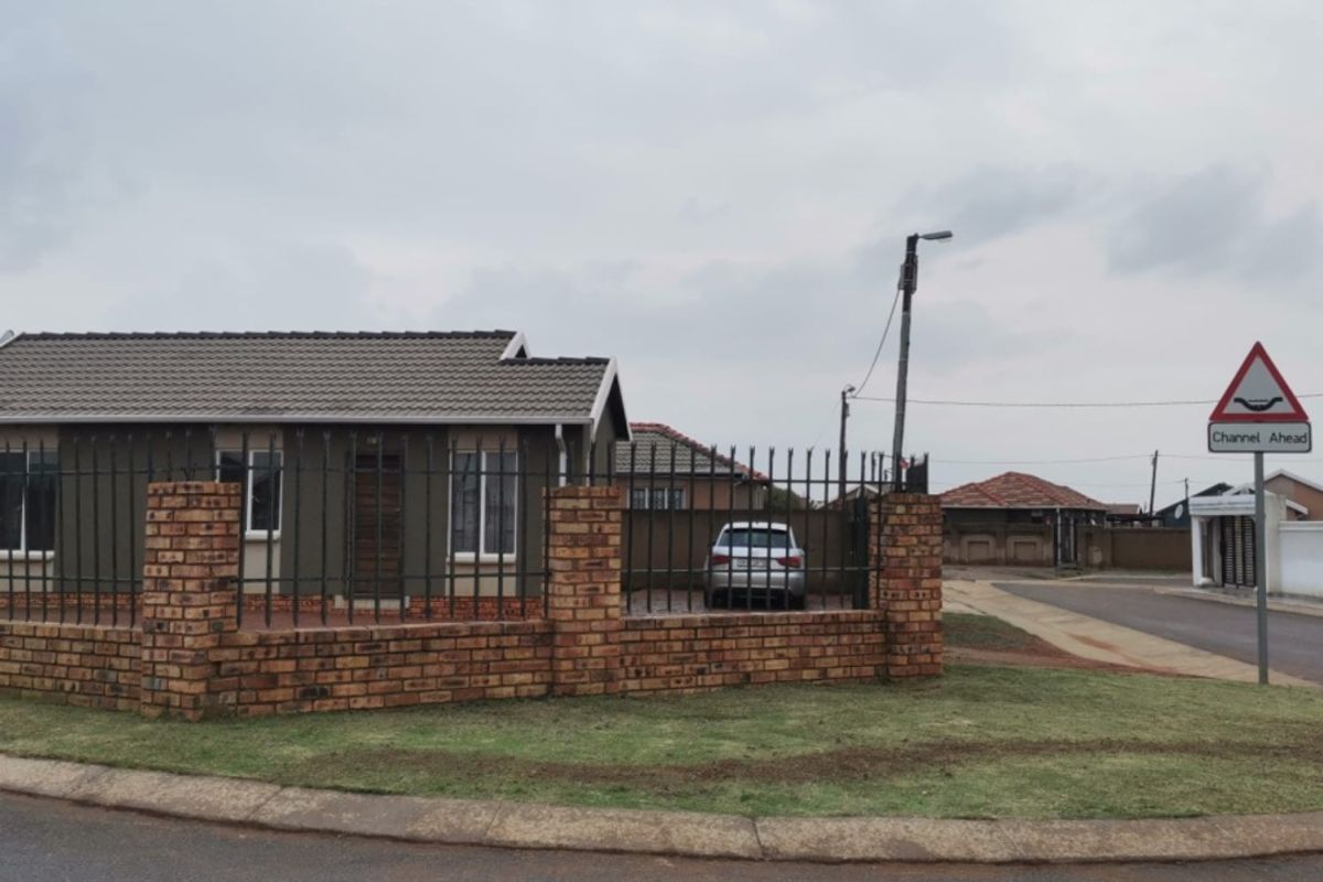 A single-story residential house featuring a brick perimeter wall, metal security fencing, and a tiled roof, situated on a corner lot.