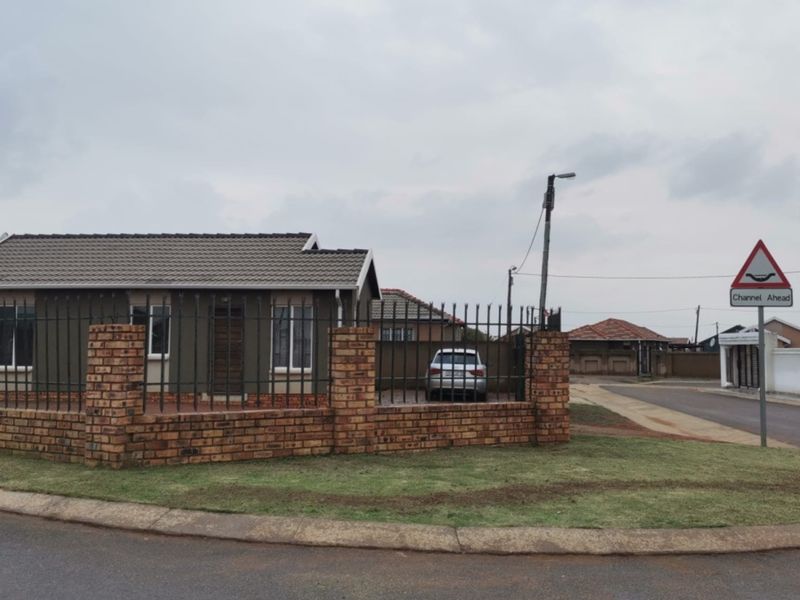 A single-story residential house featuring a brick perimeter wall, metal security fencing, and a tiled roof, situated on a corner lot.