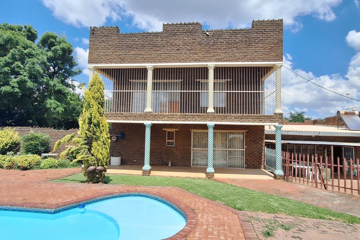 Rear view of a double-story brick residence featuring a swimming pool, paved patio area, and an upper-level balcony with security bars.