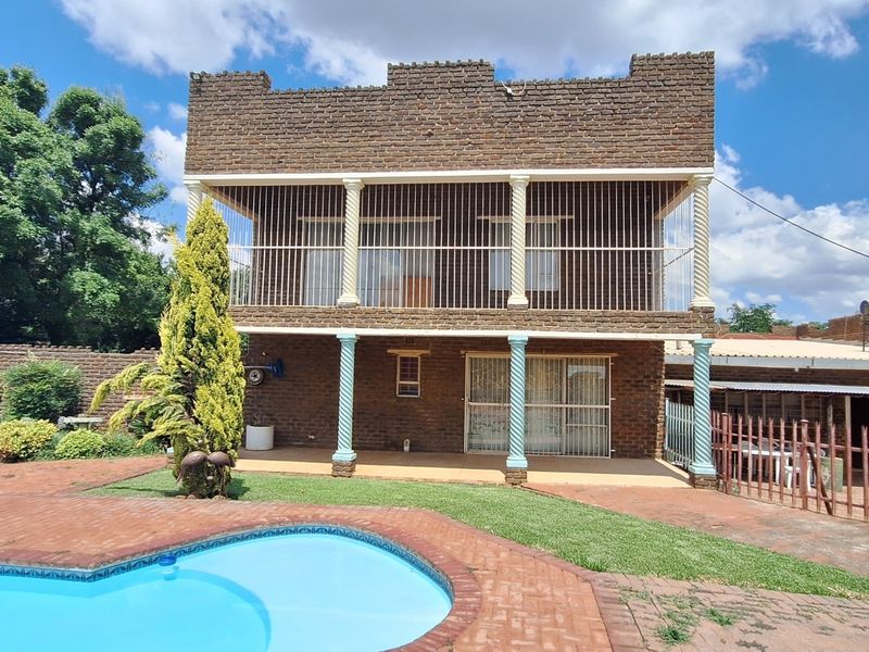 Rear view of a double-story brick residence featuring a swimming pool, paved patio area, and an upper-level balcony with security bars.