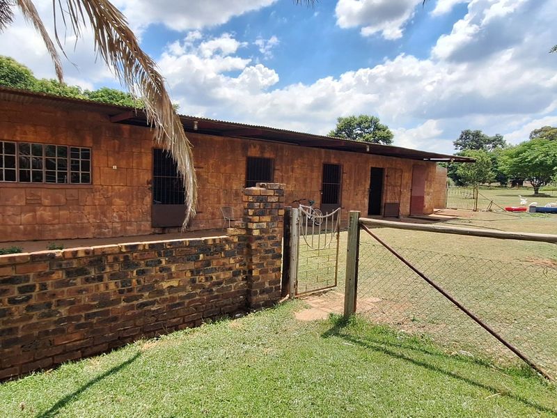 Rear view of a rustic outbuilding featuring brick construction, corrugated metal roofing, and secure metal-framed windows, set within a fenced small holding garden.