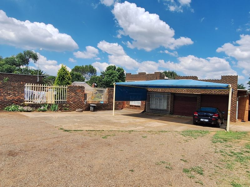 Front exterior view of the small holding featuring a face-brick boundary wall, multiple garage bays, and a large shade-cloth carport area.