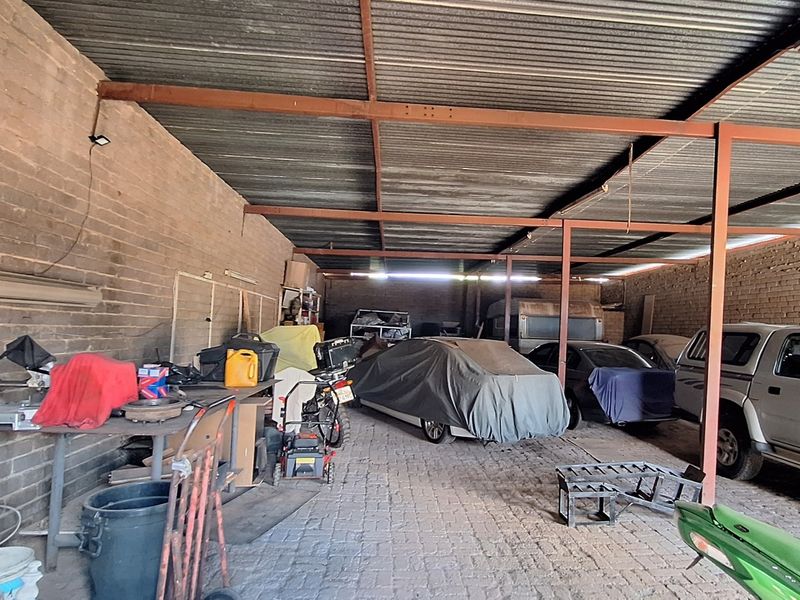 A spacious, open-sided garage featuring exposed brick walls, a corrugated metal roof, and durable paved flooring, suitable for vehicle storage or workshop use.