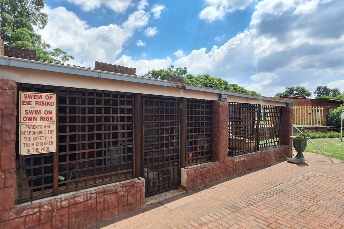 A secured pool area featuring brick masonry pillars, lattice security fencing, and brick paving, with visible signage regarding pool safety.