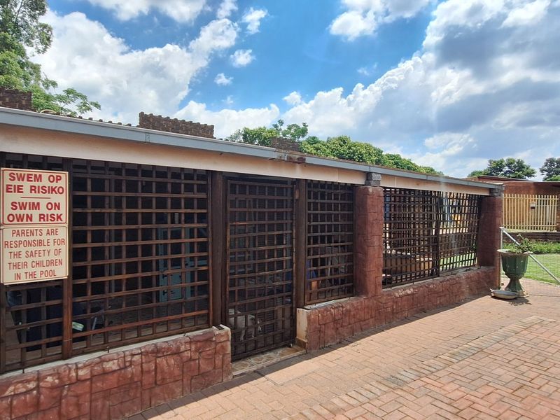 A secured pool area featuring brick masonry pillars, lattice security fencing, and brick paving, with visible signage regarding pool safety.