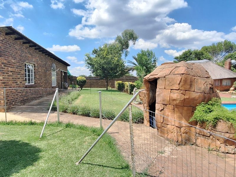 Rear view of the property featuring a swimming pool, landscaped garden, brick dwelling, and a unique rock feature structure.