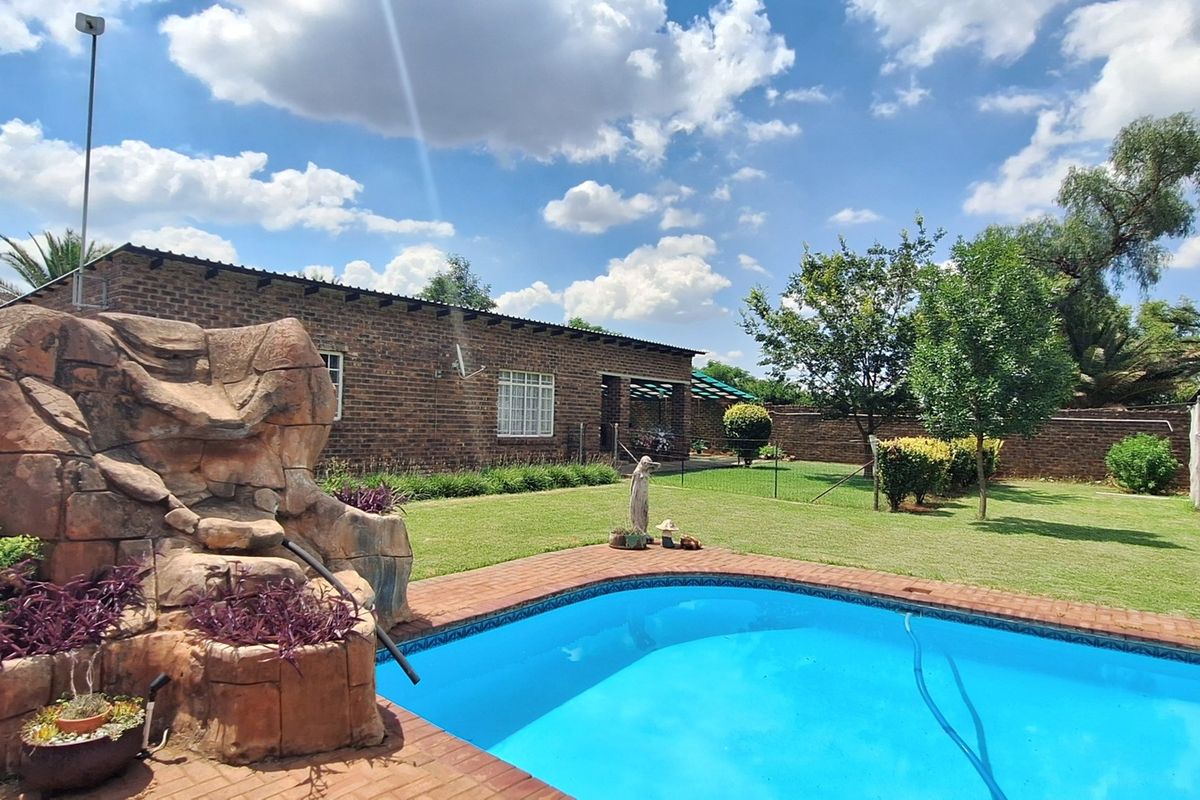 Outdoor pool area featuring a rock water feature, brick paving, and a well-maintained lawn set against a brick-walled garden.