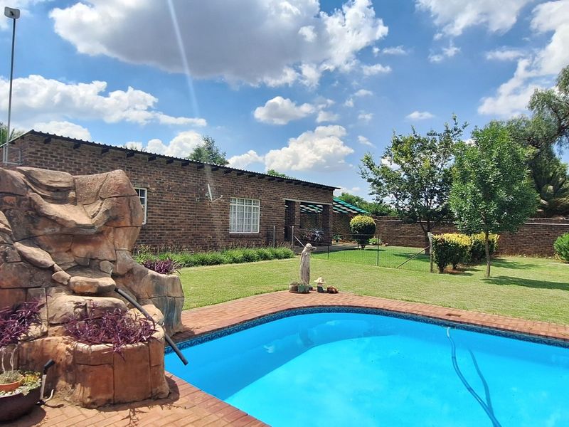 Outdoor pool area featuring a rock water feature, brick paving, and a well-maintained lawn set against a brick-walled garden.