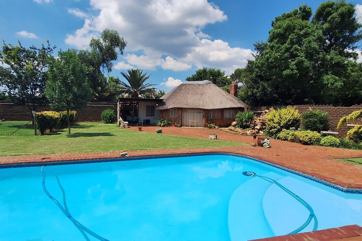 A spacious outdoor area featuring a swimming pool, well-maintained lawn, and a traditional thatched roof lapa, perfect for outdoor entertaining.