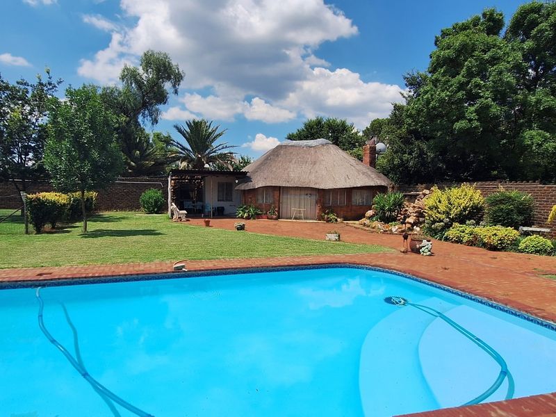 A spacious outdoor area featuring a swimming pool, well-maintained lawn, and a traditional thatched roof lapa, perfect for outdoor entertaining.