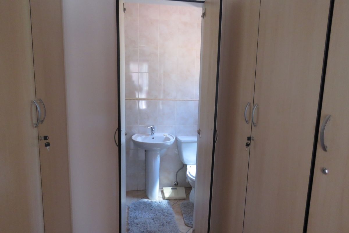 A functional bathroom featuring a pedestal basin and toilet, accessed through a hallway lined with built-in storage cupboards.