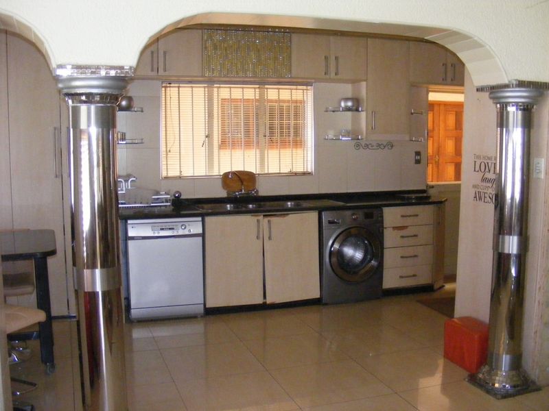A functional kitchen featuring built-in cabinetry, tiled flooring, and integrated appliances, framed by decorative metallic columns.