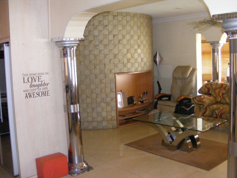 Living room featuring a unique stone-clad curved feature wall, decorative chrome columns, and tiled flooring, creating a distinct architectural focal point.