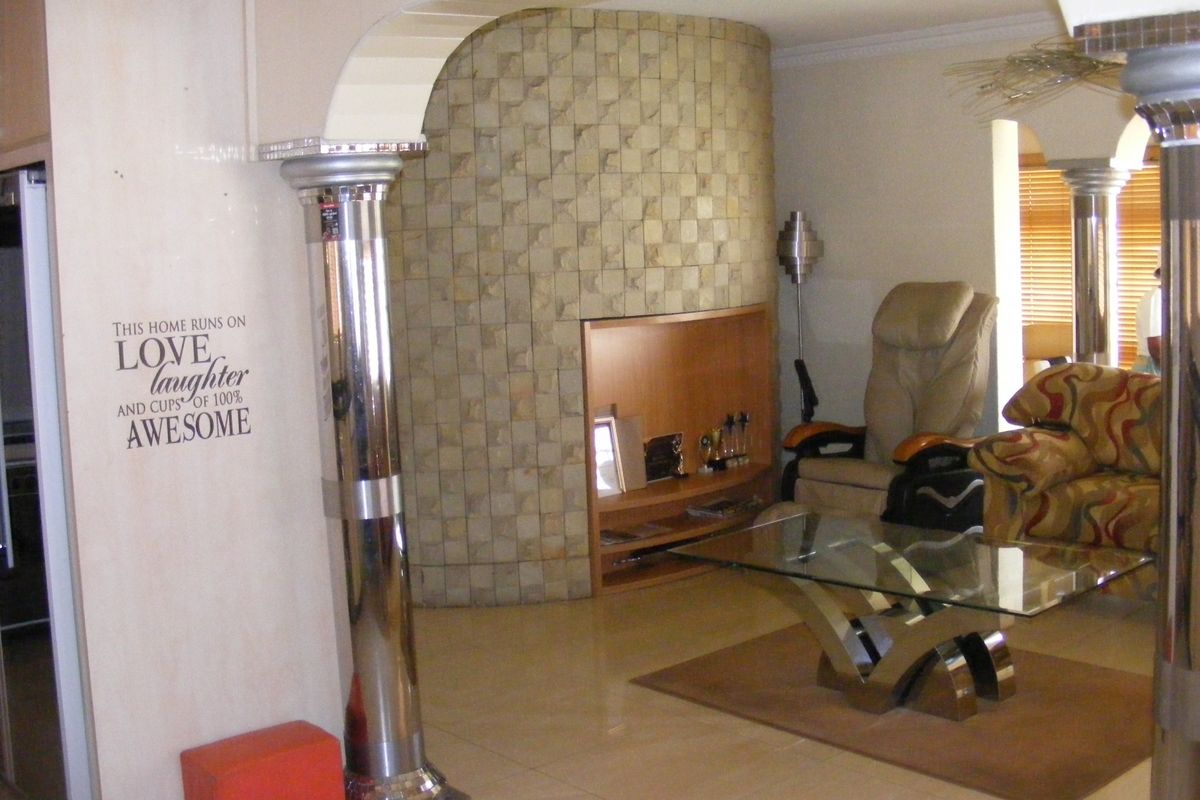 Living room featuring a unique stone-clad curved feature wall, decorative chrome columns, and tiled flooring, creating a distinct architectural focal point.