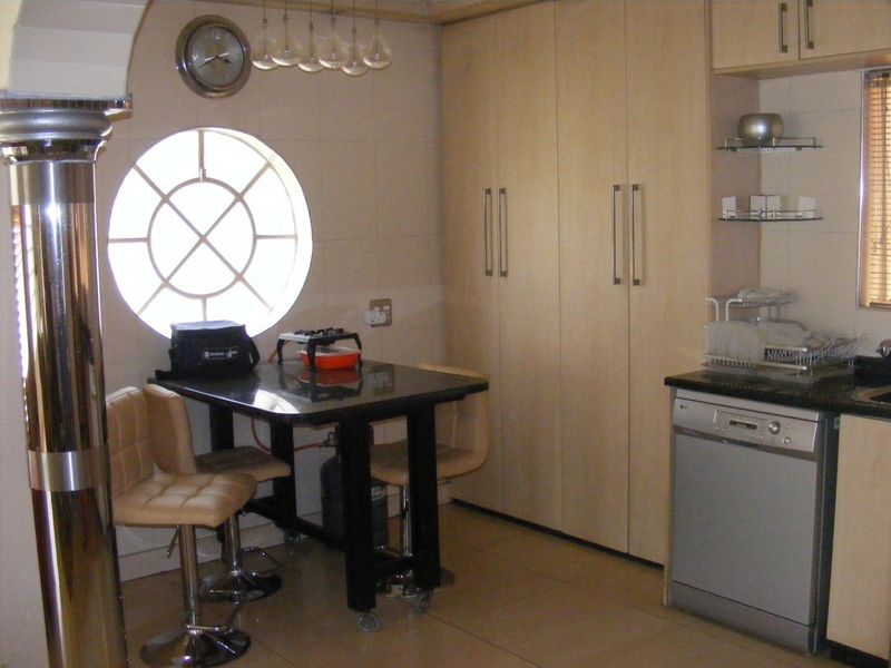 A functional kitchen area featuring light wood cabinetry, tiled flooring, a unique circular window, and an integrated dishwasher.