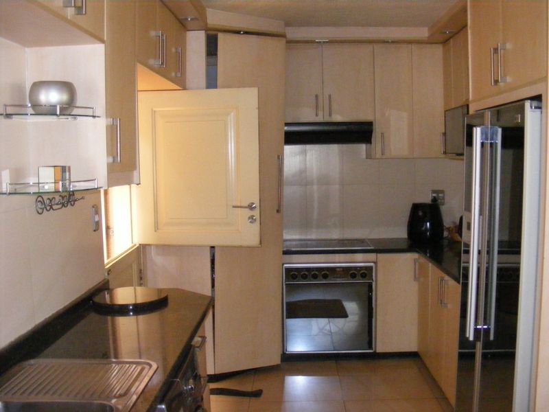 Compact kitchen featuring light-toned cabinetry, granite countertops, integrated oven and hob, and tiled flooring.
