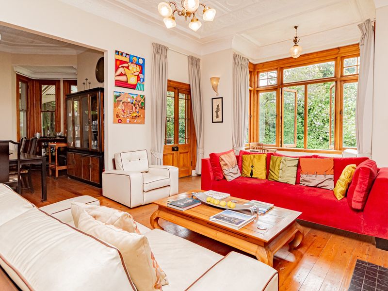 Spacious open-plan living and dining area featuring classic timber flooring, ornate ceiling details, and large timber-framed windows providing natural light and garden views.