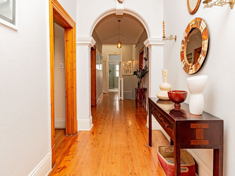 A bright and welcoming hallway featuring polished timber flooring, classic archway detailing, and high ceilings, providing a seamless transition between living spaces.