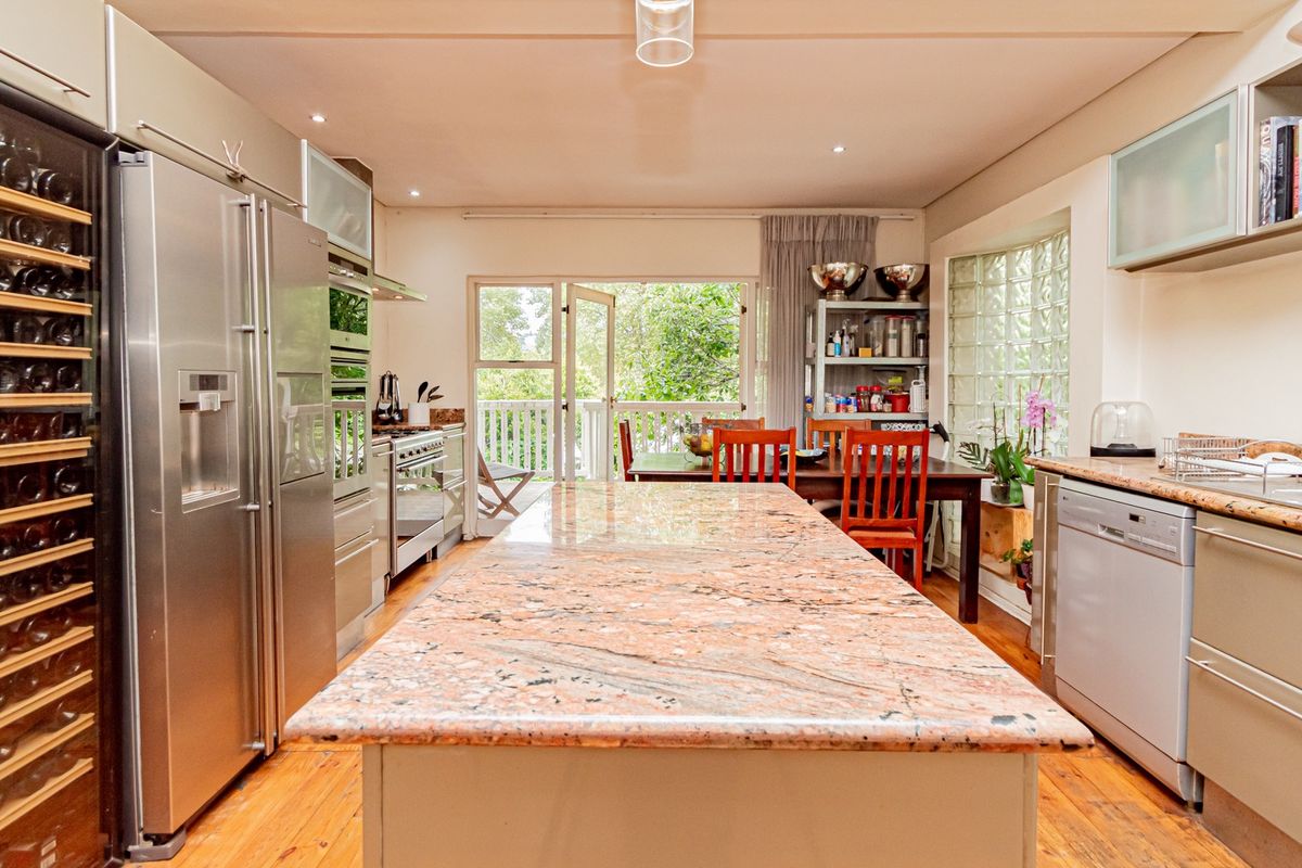 Spacious kitchen featuring a large granite island, stainless steel appliances, built-in wine storage, and direct access to an outdoor patio area.