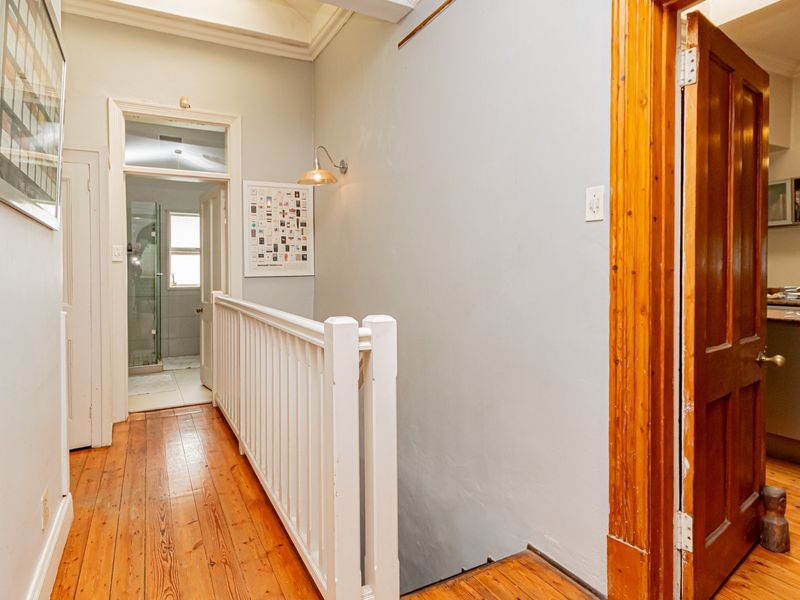 A bright hallway featuring polished timber flooring, a white balustrade, and a skylight, providing access to adjacent rooms including a bathroom and kitchen area.