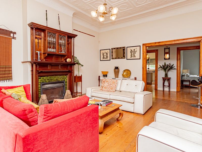 Spacious living room featuring original hardwood floors, an ornate timber fireplace mantel with tiled surround, and classic decorative ceiling molding.