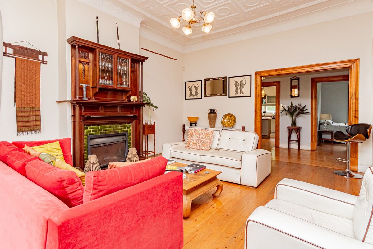 Spacious living room featuring original hardwood floors, an ornate timber fireplace mantel with tiled surround, and classic decorative ceiling molding.