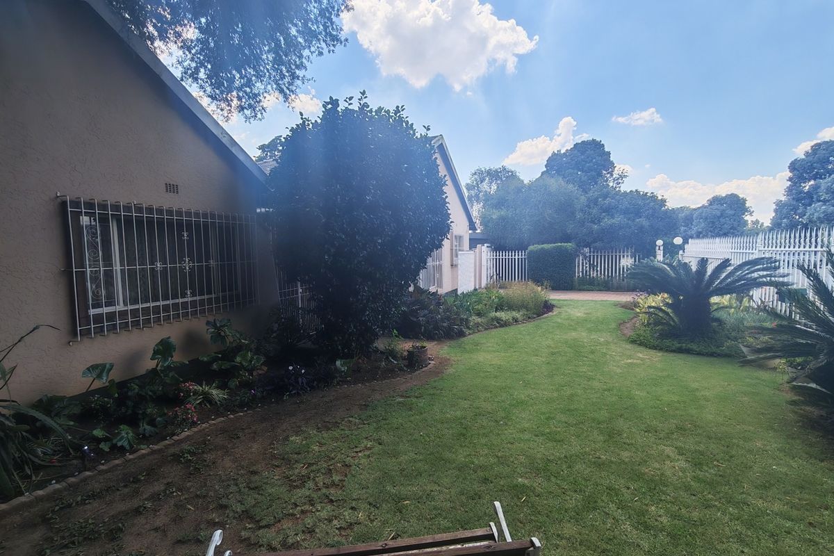 A well-maintained rear garden featuring a manicured lawn, established garden beds, and secure perimeter fencing along the side of the house.