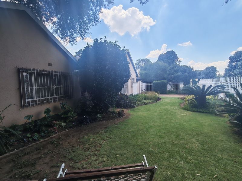 A well-maintained rear garden featuring a manicured lawn, established garden beds, and secure perimeter fencing along the side of the house.