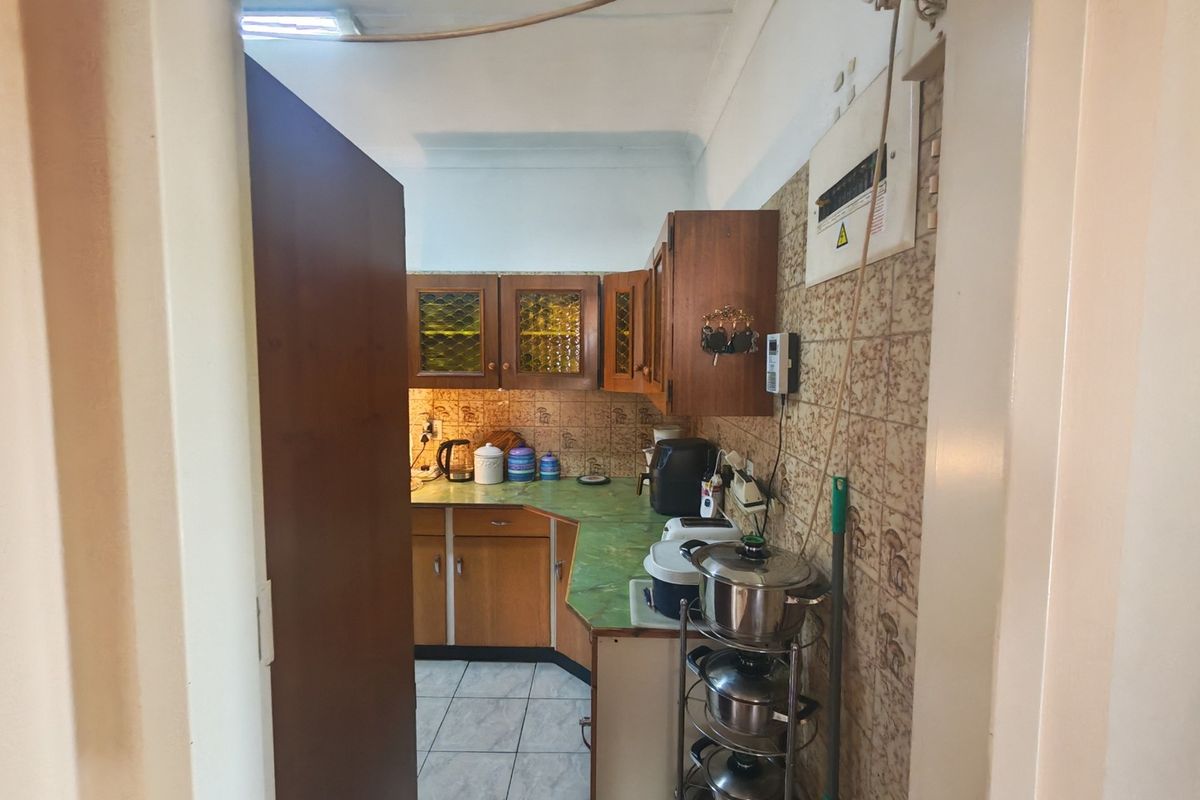 A compact kitchen featuring dated wooden cabinetry, laminate countertops, and tiled finishes, requiring modernization to improve functionality and aesthetic appeal.