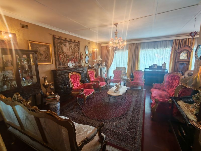 A traditional living room featuring a stone fireplace, hardwood flooring, and a central chandelier, offering a classic and formal atmosphere.