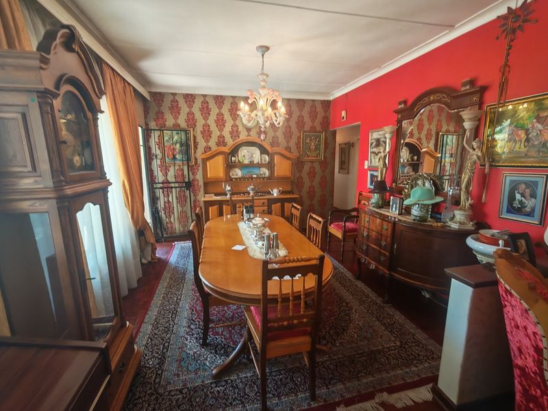 A formal dining room featuring a classic chandelier, patterned wallpaper, and a security gate, offering a traditional aesthetic.