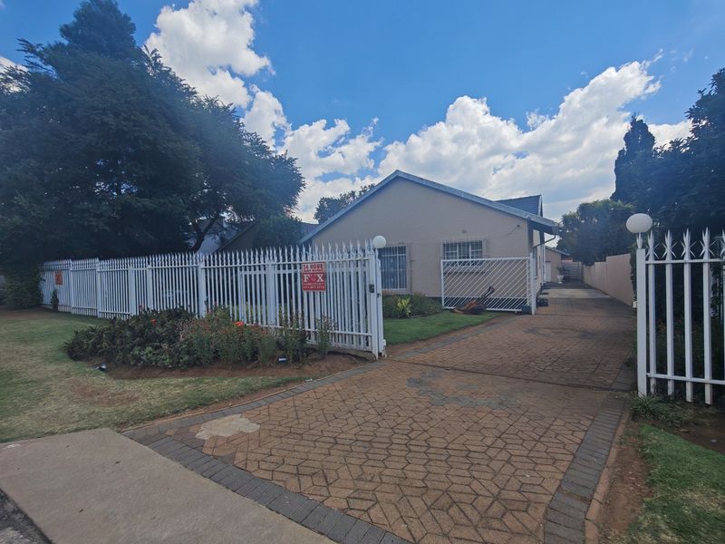 Front view of a residential property featuring a paved driveway, secure metal fencing, and a gated entrance with security bars on the windows.