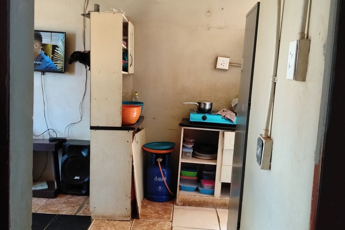 A compact kitchen area featuring tiled flooring and basic cabinetry, currently showing significant wear and exposed electrical wiring throughout the space.